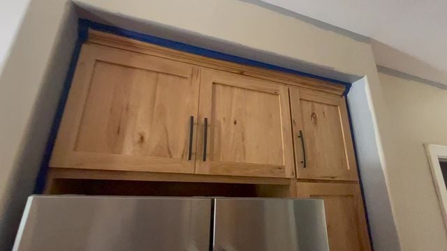 wooden cabinets above a fridge and wall being painted tan