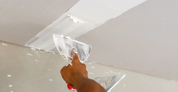 Five Star Painting professional adding mud to repair drywall on a ceiling.
