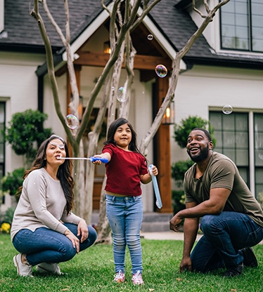 Family of three playing with bubbles on front lawn of residential home.