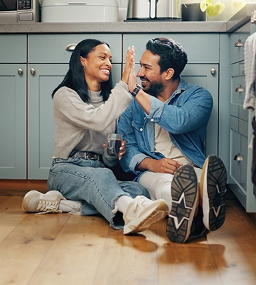 Couple doing a high-five on floor of kitchen with painted cabinets.