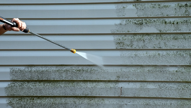 View of someone pressure washing dirty siding on a home.