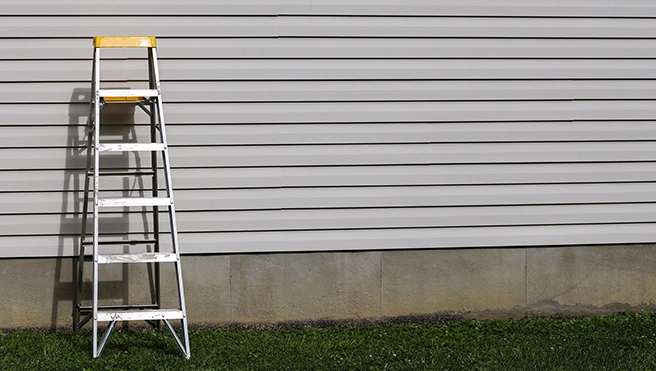 A ladder leaning against a home's vinyl siding.
