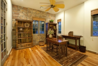 Earth-toned home office with taupe paint, brown brick wall, wooden desk, wooden bookshelves and hardwood floors.