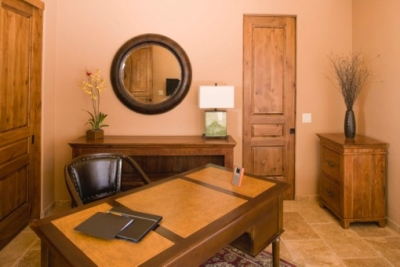 Beige walled office with medium colored wood furniture, dark wood accents and personal touches including a painting, flower arrangements and mirror.