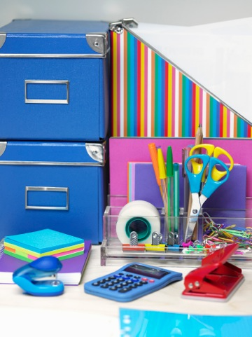 Brightly colored office supplies including folders, scissors, sticky notes, small stapler, pens, tap, three whole punch and more.