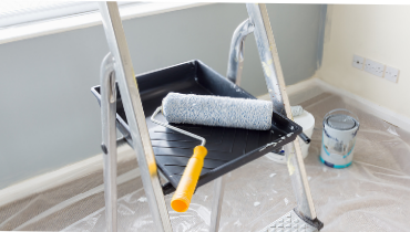 Photo of a room covered in protective plastic, a painting tray and roller brush rests on top of a painting ladder