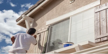 Man in white shirt painting wooden window shutters