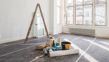 Painting supplies and ladder in the middle of a empty room.