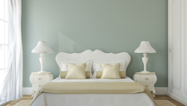 Photo of a bedroom with light colored furniture against a sage green wall