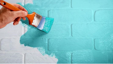 Photo of someone painting a white brick wall turquoise.