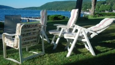 Photo of four empty lawn chairs on a lawn, in the distant is a large blue body of water and distant green hills