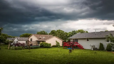 Grassy backyard and several homes under cloudy sky.