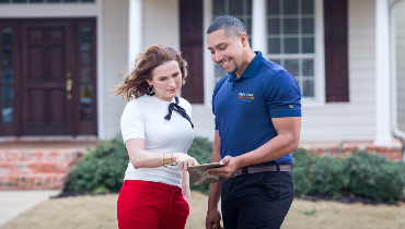 Photo of a woman and a Five Star Painting employee discussing paperwork on the front lawn of a large house