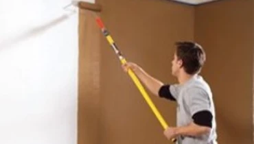 Painter with roller brush painting the wall brown.