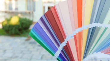 Photo of a fan of paint swatches, in the background is a blurred view of the front of a house
